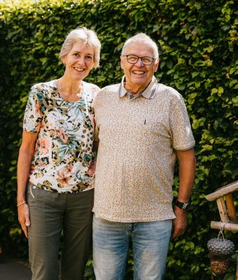 Het echtpaar Anja en Theo staan lachend in hun tuin op de foto