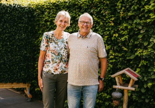 Het echtpaar Anja en Theo staan lachend in hun tuin op de foto