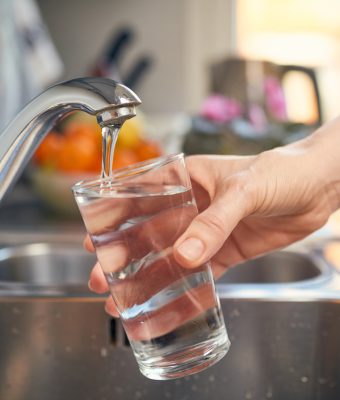 Een glas water vullen bij de kraan in de keuken